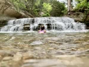 Girl sitting in the water in front of a waterfall near Fort Hood, Texas.