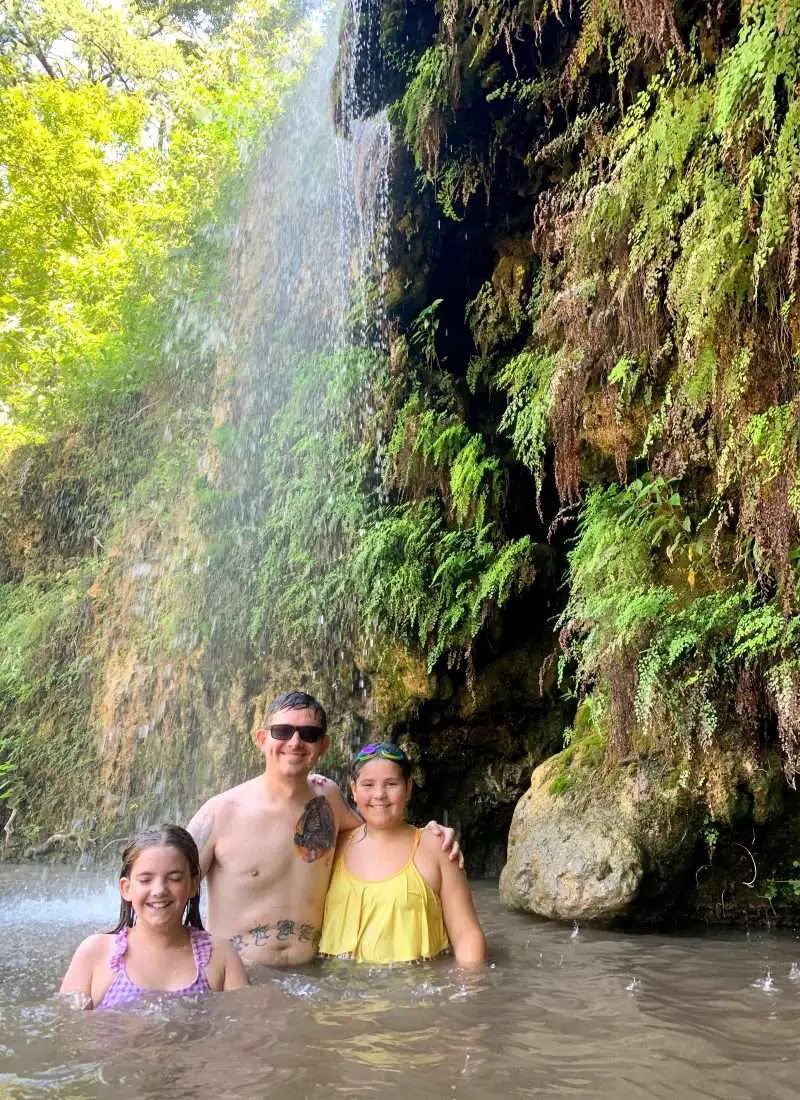 Family swimming under waterfall at Krause Springs in Spicewood, Texas.