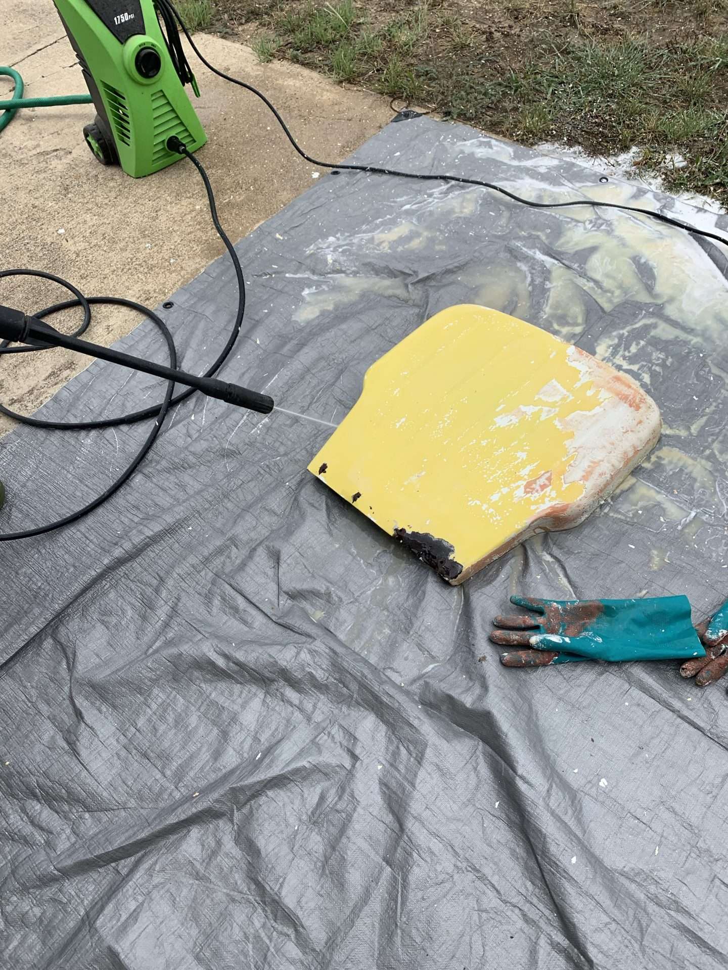 Using a pressure washer to blast the paint stripper and layers of paint off of a vintage metal glider.